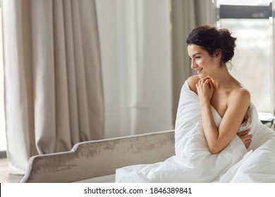 Beautiful charming smiling brunette woman relax in blanket side view. Cozy bedroom with luxury bed. Home or hotel fashion interior.