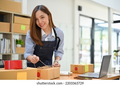 Beautiful And Charming Young Asian Female E-commerce Business Owner Packing A Shipping Package In Her Stock Room. E-commerce Business Concept