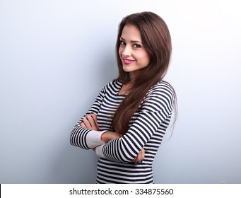 Beautiful charming young casual woman with folded hands looking happy on blue background with empty copy space