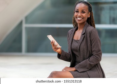 Beautiful cheerful african american executive business woman at the workspace office, holding a smartphone