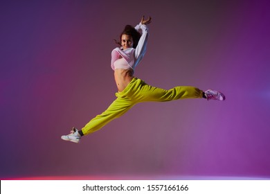 Beautiful cheerful girl jumping doing split leap in the air, looking straight at camera with joyful expression, flexible and weightless concept professional dancer in motion - Shutterstock ID 1557166166