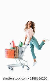 beautiful cheerful girl jumping with shopping cart and bags, isolated on white