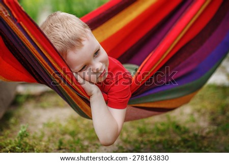 Beautiful cheerful little boy resting in a hammock striped textile