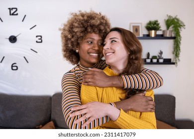 Beautiful and cheerful multiracial lesbian couple hugging and looking each other smiling. Lovely and happy homosexual women embracing at home staring each other. - Powered by Shutterstock