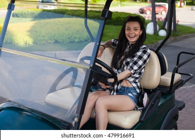 Beautiful Cheerful Woman With Glasses On Her Head In 
Plaid Shirt Is Sitting On A Green Golf Cart.