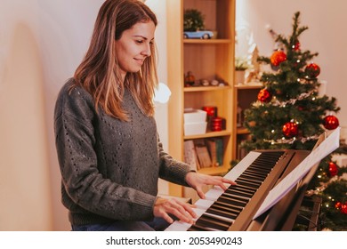 Beautiful Cheerful Woman Playing Piano Against The Background Of A Decorated Christmas Tree At Home. Christmas Lights And Music, Family Time. Holidays Concept. Merry Christmas, Happy New Year.