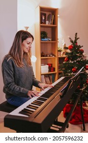 Beautiful Cheerful Woman Playing Piano Against The Background Of A Decorated Christmas Tree At Home. Christmas Lights And Music, Family Time. Holidays Concept. Merry Christmas, Happy New Year.