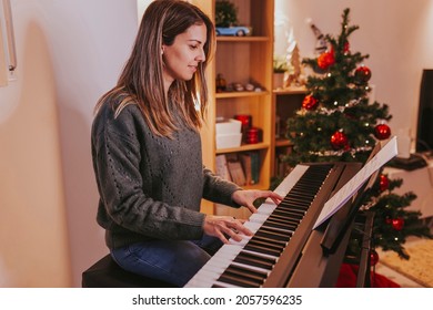 Beautiful Cheerful Woman Playing Piano Against The Background Of A Decorated Christmas Tree At Home. Christmas Lights And Music, Family Time. Holidays Concept. Merry Christmas, Happy New Year.