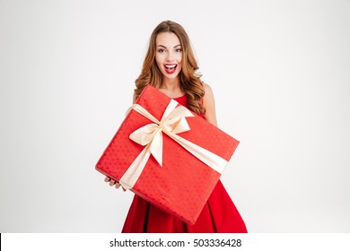 Beautiful Cheerful Woman In Santa Claus Dress Giving You Big Red Gift Over White Background