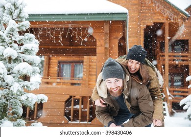 冬の丸太小屋の前で楽しみを見せる、美しく陽気な若い夫婦の写真素材
