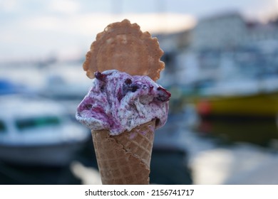 Beautiful cherry poppy seed ice cream in waffle cone in front of Rovinj port. Ice cream in girl hand on background of sea and boats .