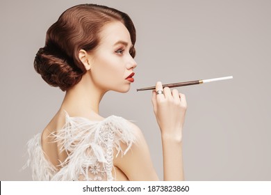 Beautiful chic woman in a luxury white dress smoking a cigarette in the mouthpiece. Evening makeup and hairstyle of the 20s. Hollywood style.