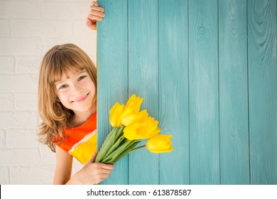 Beautiful Child With Bouquet Of Flowers Hiding Behind Wooden Background. Spring Family Holiday Concept. Mother's Day