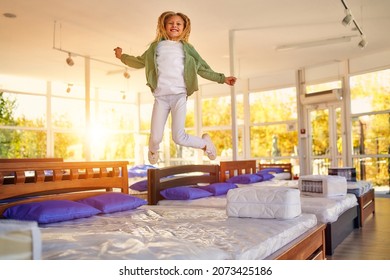 Beautiful child cute girl jumping on the bed and having fun in the store. Purchase of bedding, mattress and bed.