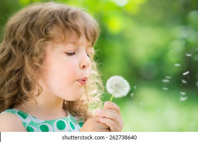 Beautiful Child With Dandelion Flower In Spring Park. Happy Kid Having Fun Outdoors