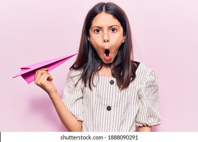 Beautiful Child Girl Holding Paper Airplane Scared And Amazed With Open Mouth For Surprise, Disbelief Face 