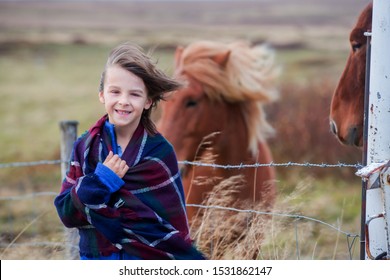 Beautiful child and horses in the nature, early in the morning on a windy autumn day in Iceland