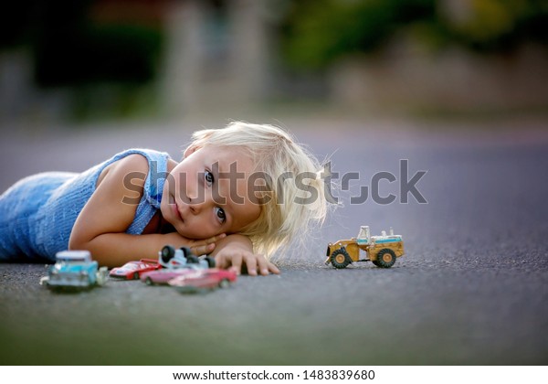 Beautiful child, playing with car toys on\
sunset on a quiet village street,\
summertime