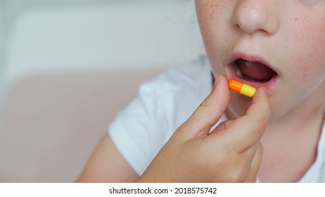 Beautiful Child Is Putting Medicine To Mouth. Little Girl Taking Pill. Pretty Child Face, Capsule In Hand, Pink Blurred Background, Close Up. Treatment Of The Child. Oral Therapy, Pedriatric Medicine.