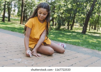 beautiful child sitting and drawing with chalk in park