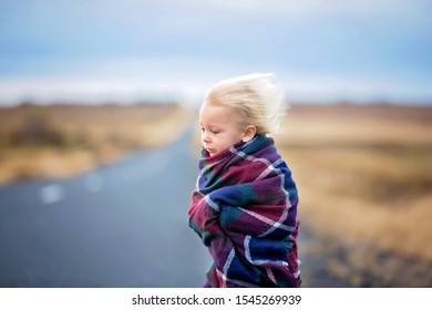 Beautiful child, standing on a road on a very windy day, wrapped in scarf, watching the sunrise in Iceland, autumntime