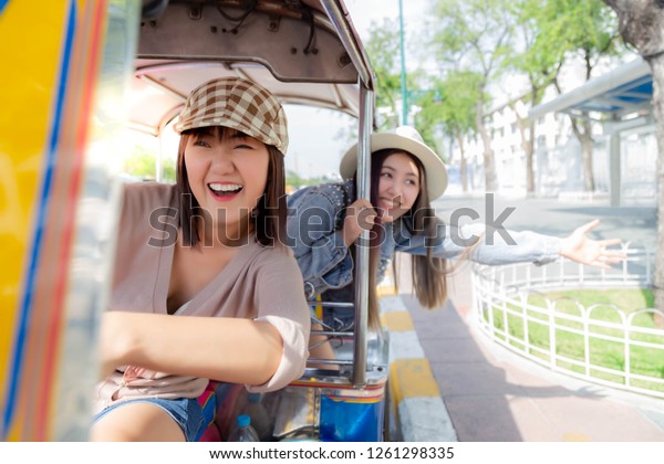 Beautiful Chinese or Japanese woman drive auto\
rickshaw and her Thai friend is sitting behind her. They are closed\
friend and always travel together. They’re going to touristic place\
with happy faces