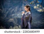 A beautiful Chinese woman dressed in Hanfu is playing a flute under a pear tree on a hill