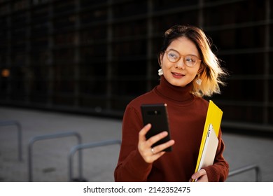 Beautiful Chinese Woman With Mobile Phone Walking On The Street. Young Girl Typing A Message