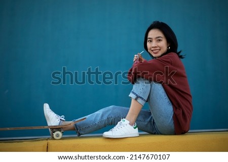 Beautiful Chinese woman with skateboard. Portrait of urban young girl outdoors