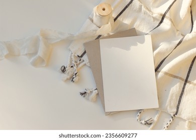 Beautiful Christmas or autumn  stationery. Closeup of blank greeting card, invitation  mockup. Checkered plaid blanket and silk ribbon on white table in sunlight. Flatlay, top view. Copy space. - Powered by Shutterstock