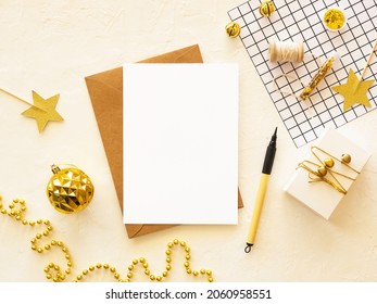 Beautiful Christmas Card Mockup With Blank Card On Table Decorated With Golden Xmas Decorations, Craft Paper Envelope,top View. Copy Space For Your Design Or Winter Sale Promotion