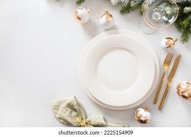 Beautiful Christmas Festive Table Setting With White Plate, Golden Balls And Napkin Ring As Deer On White Background. View From Above. Copy Space. Xmas Festive Dinner.