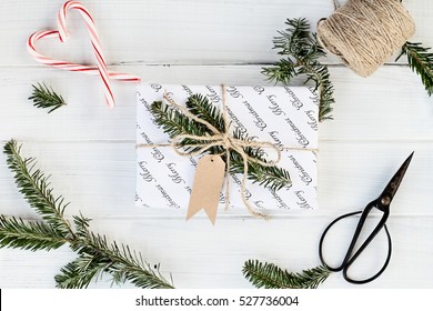 Beautiful Christmas gift with blank tag. Decorated naturally with pine tree twigs and twine over a white background with candy canes. Image shot from above.