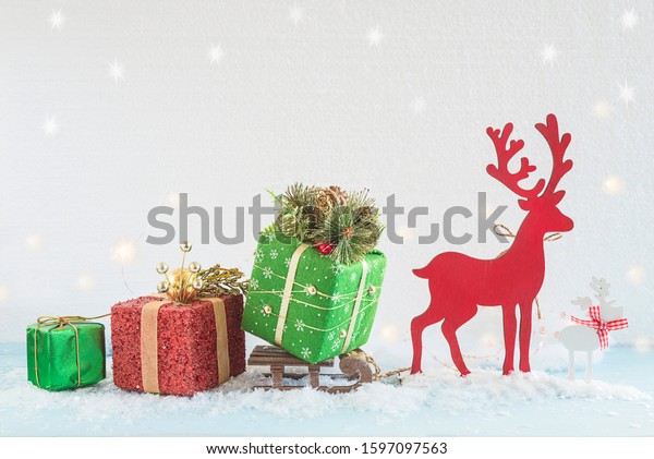 Beautiful Christmas holiday and New year\
greeting card. Red deer carring a sled with various gift boxes on\
the fresh snow\
background