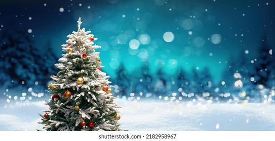 Beautiful Christmas and New Year's background with decorated Christmas tree in fluffy snowdrifts against background of evening winter forest, falling snow and magical sky.