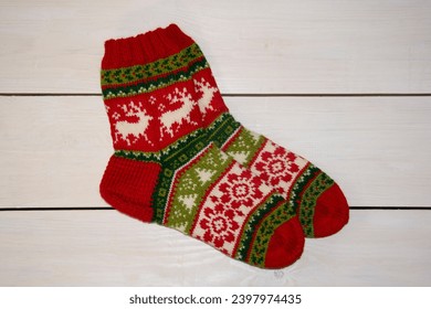 Beautiful Christmas socks with designs of reindeer, trees and flowers, hand knitted from wool yarn in red, green and white colors on a background of white boards. - Powered by Shutterstock