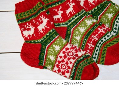 Beautiful Christmas socks with patterns of reindeer, fir trees, snowflakes and flowers, hand knitted from red, green and white wool yarn on a background of white painted boards. Handmade. - Powered by Shutterstock