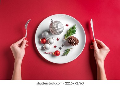 Beautiful Christmas Table Setting And Female Hands.  Festive Silver Baubles And Pine Cone On White Plate On Red Background, Flat Lay. Christmas Dinner, Party Design, Menu Concept.