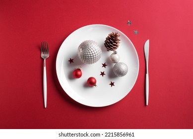 Beautiful Christmas Table Setting.  White Plate, Cutlery With And Festive Ornaments On Red Background, Flat Lay, Copy Space. Christmas Dinner, Party Design, Menu Concept.