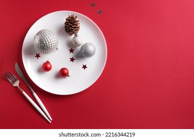 Beautiful Christmas Table Setting.  White Plate, Cutlery With And Festive Ornaments On Red Background, Flat Lay, Copy Space. Christmas Dinner, Party Design, Menu Concept.