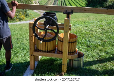 Beautiful Cider Press On A Hillside With A Farm In The Background. Young African Americna Man Turns The Crank On The Press. Shot In Natural Light With Copy Space.