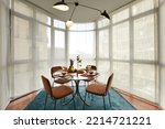 Beautiful circular beveled edge clear glass dining table with crockery of fresh fruit and sweet desserts, brown velvet upholstered chairs and bay window with blinds