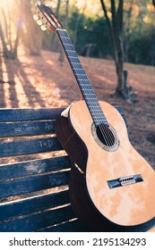 Beautiful classical guitar on a bench in the park with lens flare. Photo of a new wooden guitar with nylon strings outdoors in the summer during sunset. No people. Beautiful string instrument. - Shutterstock ID 2195134293