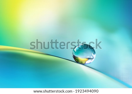 Beautiful clean transparent bright drop of water on smooth surface in blue and yellow colors, macro. Creative image of beauty of environment and nature.