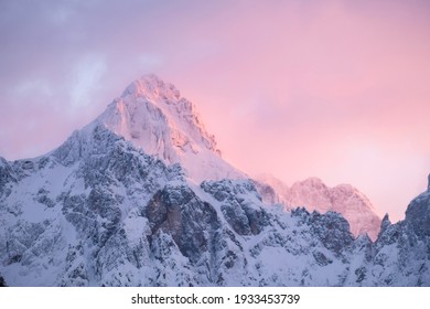 Beautiful close up shot of a pink glowing Mountain top in the Alps at sunset while wind is blowing snow off the Mountain into pink and purple clouds. Power of natural elements in an alpine surrounding - Shutterstock ID 1933453739