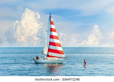 Beautiful clouds in the background. A boat with a red and white sail meets the surfer in the blue sea. Amazing concept design for outdoor recreation. Summer water sports, outdoor adventure