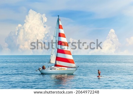 Beautiful clouds in the background. A boat with a red and white sail meets the surfer in the blue sea. Amazing concept design for outdoor recreation. Summer water sports, outdoor adventure