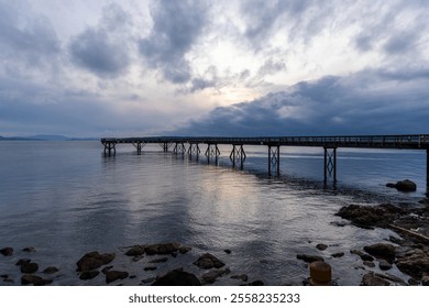 A beautiful coastal pier stretches over calm waters under a clouded sky during sunset, creating a serene and peaceful atmosphere for contemplative moments. - Powered by Shutterstock