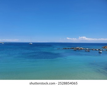 Beautiful coastal scene in Zakynthos, Greece, with clear turquoise waters, a sailboat, and small boats near a rocky shore. Captured in September, highlighting the island's stunning seascape. - Powered by Shutterstock