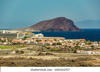 Beautiful Coastal View Of Montana Roja (Red Mountain) Mountain In Tenerife. Part Of Gran Canaria Island In A Light Haze In The Background. Hot Sunny Day With Clear Blue Sky. Long Focus Lens Shot.